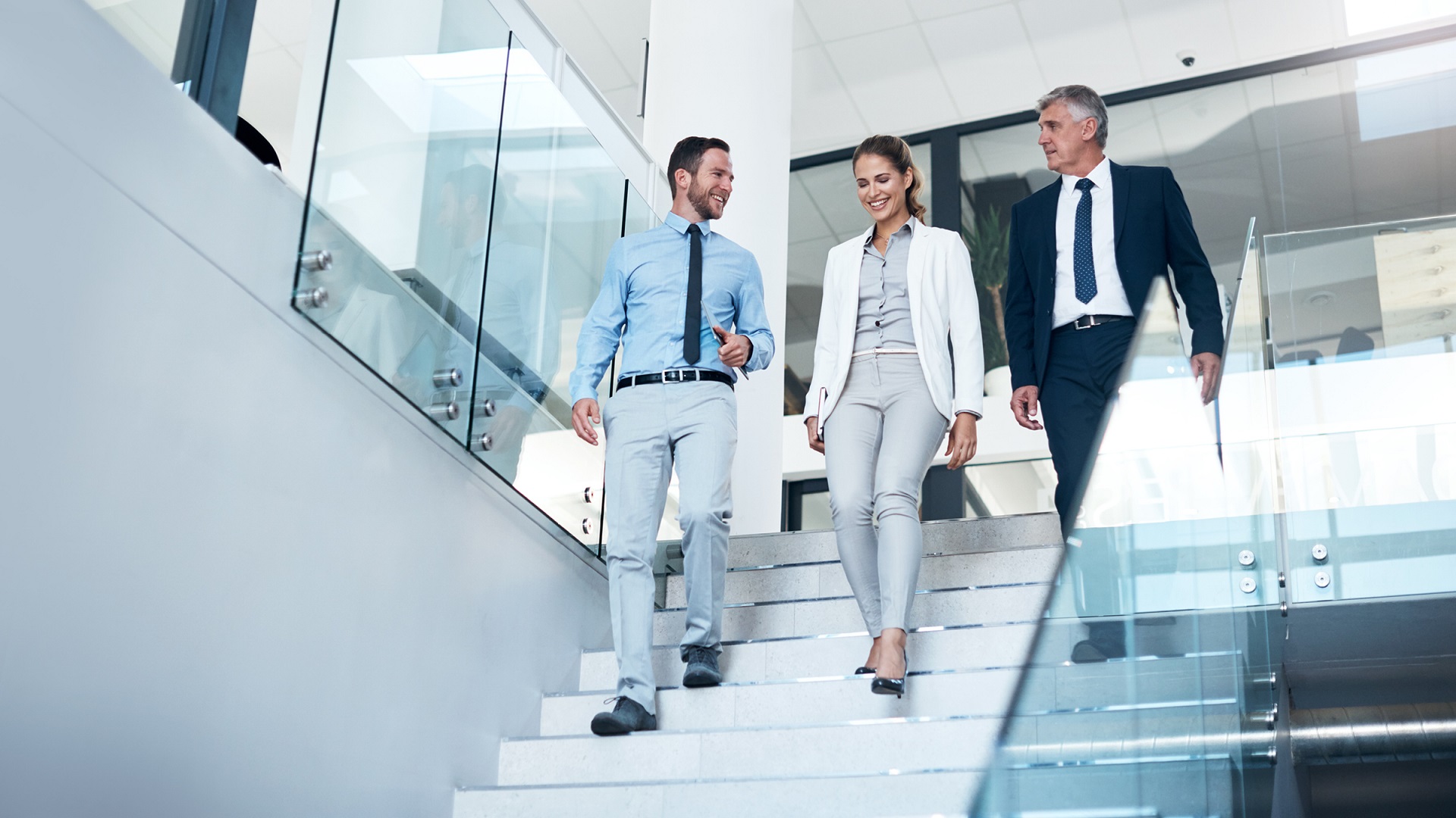 Three businesspeople walking down stairs in a glass building