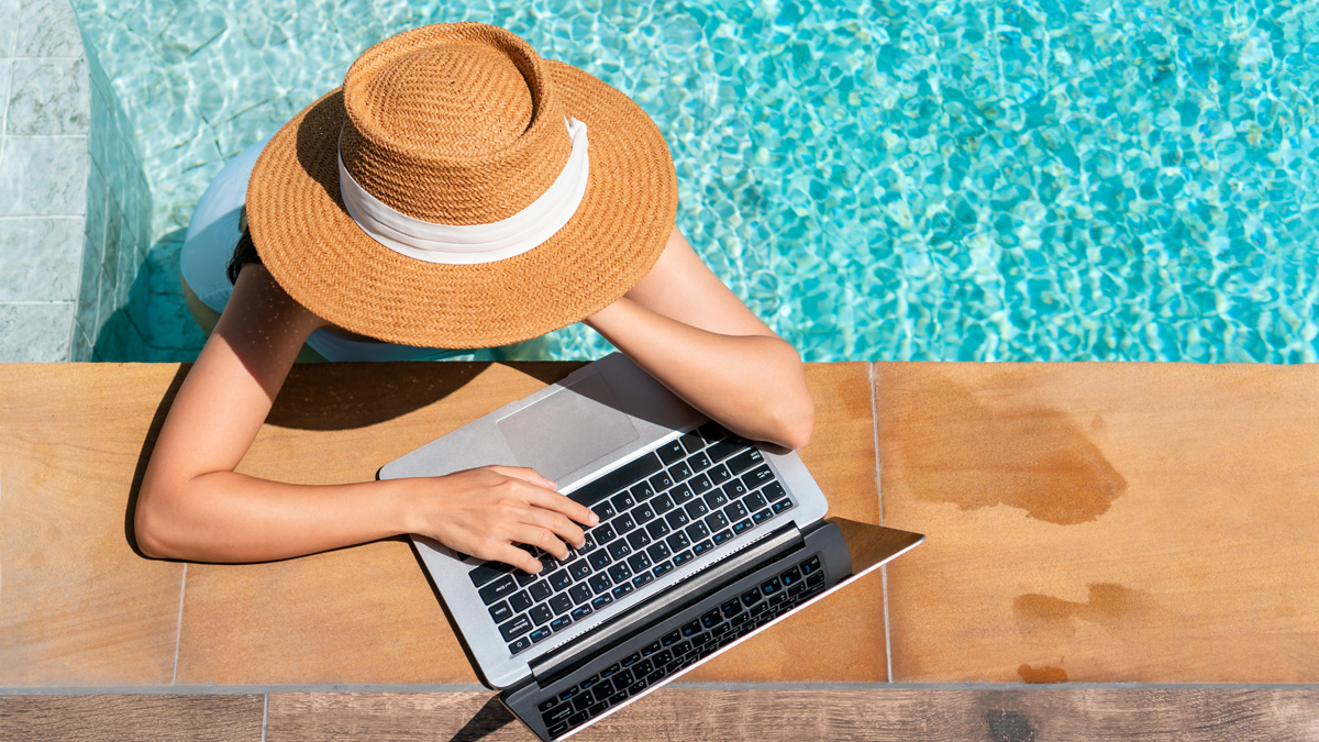 A woman, poolside, types on her laptop.